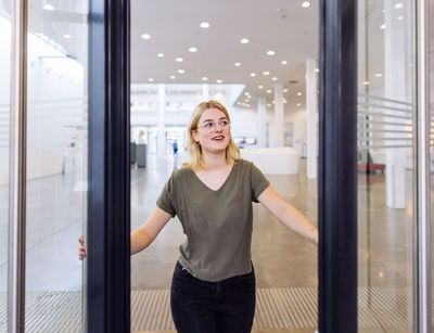 Studentin öffnet mit einem Lächeln die Tür zum Neuen Augusteum, Foto: Christian Hüller