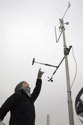 Student stands outside and points to a large metereological measuring device