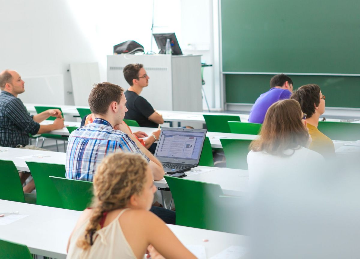 enlarge the image: Studierende sitzen im Hörsaal an Tischen verteilt und folgen einer Vorlesung